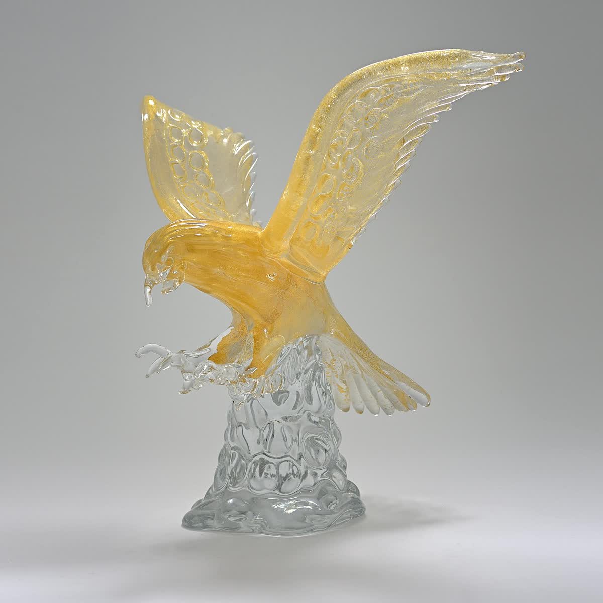 Falco: scultura in vetro ambra con ali spiegate, posato su una base di vetro trasparente
