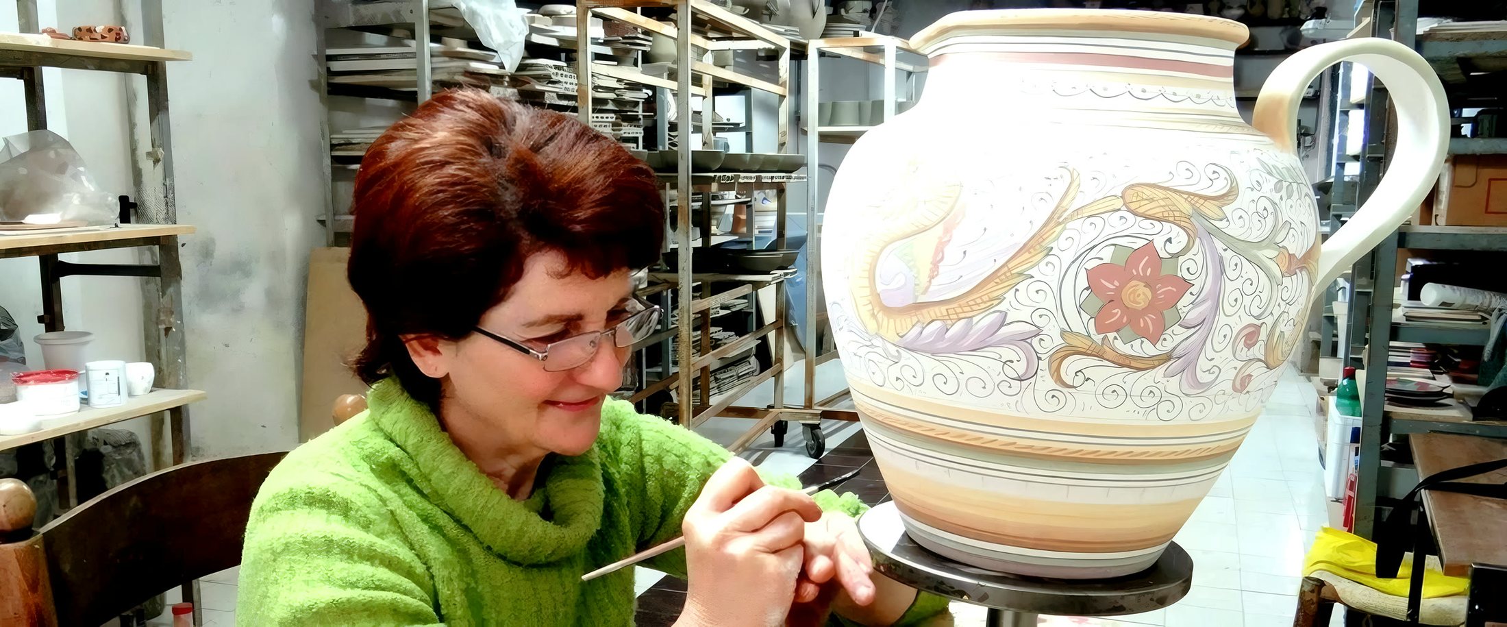 In laboratorio: la decorazione a mano libera di una grande anfora, fra gli scaffali dei pezzi in attesa di cottura