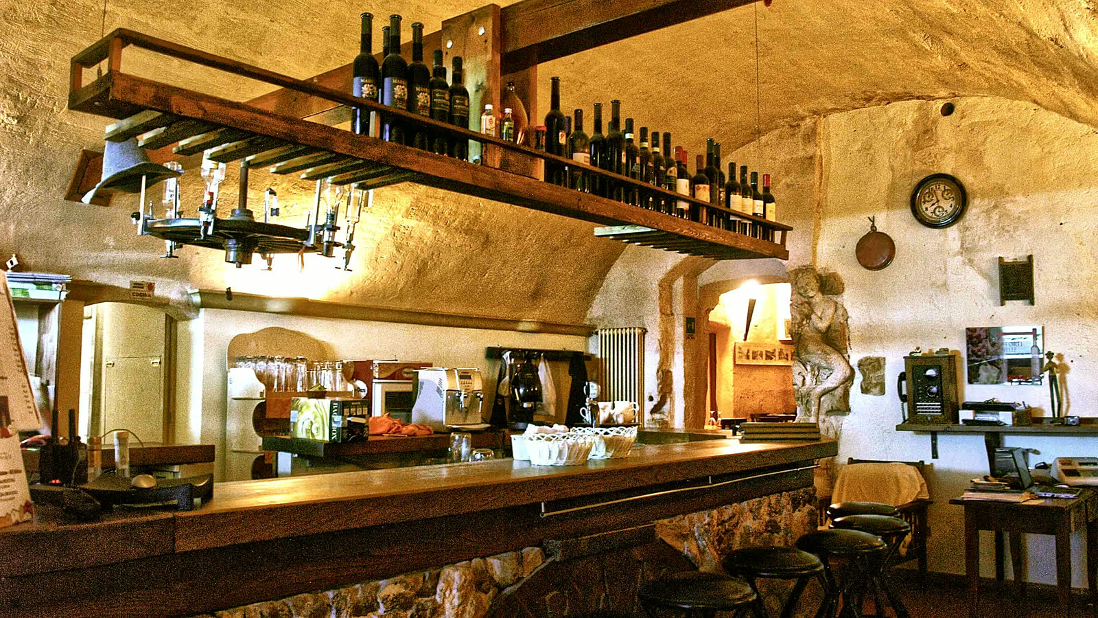 Il bancone della trattoria nella sala scavata, con la rastrelliera dei vini lucani